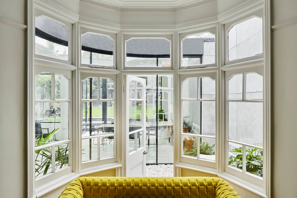 Elegant room with yellow tufted sofa, large bay window, and outdoor greenery view.