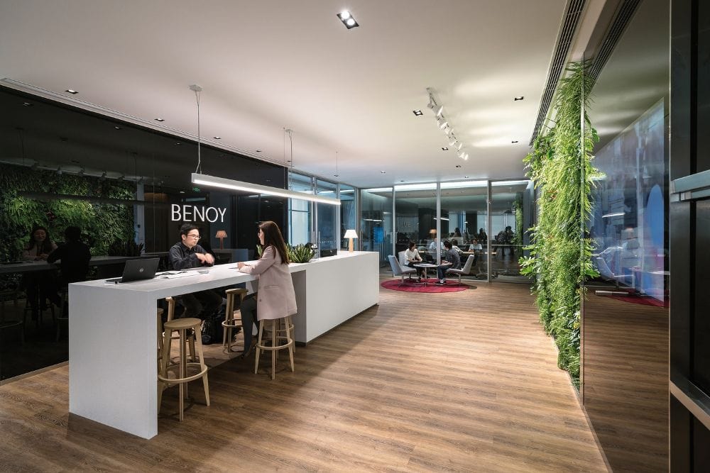 Modern office reception at Benoy with vertical garden, glass-walled meeting room, and wood-like flooring.