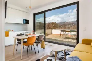 Bright modern living space with kitchen, dining area, and terrace, featuring urban views.