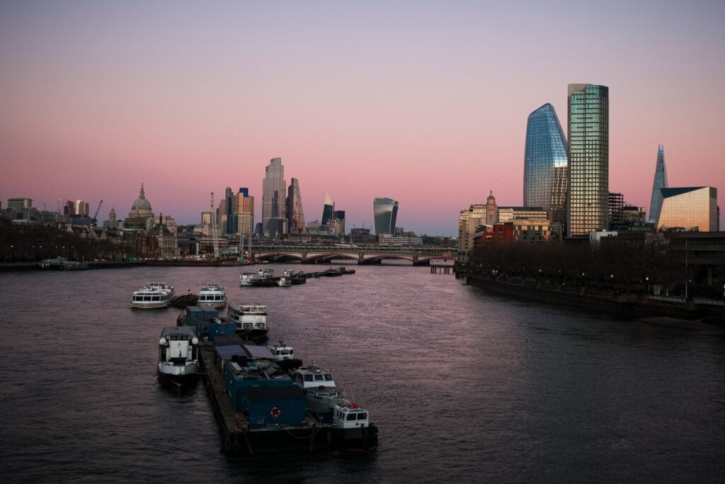 Dusk cityscape with river, boats, modern and historic buildings.