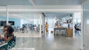 Modern, open-concept office with glass meeting room, collaborative workspaces, and kitchenette for employee comfort.