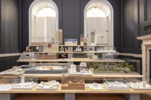 Exhibition room displaying detailed architectural models with natural light from arched windows.