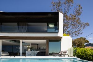 Modern two-story house with large glass windows, pool, and stylish outdoor lounge area.