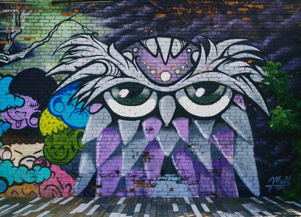 Vibrant graffiti mural with an abstract owl and colourful faces on a textured brick wall.