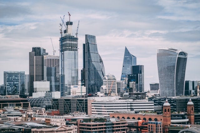 Modern city skyline with historical clock tower and glass skyscrapers under a cloudy sky.