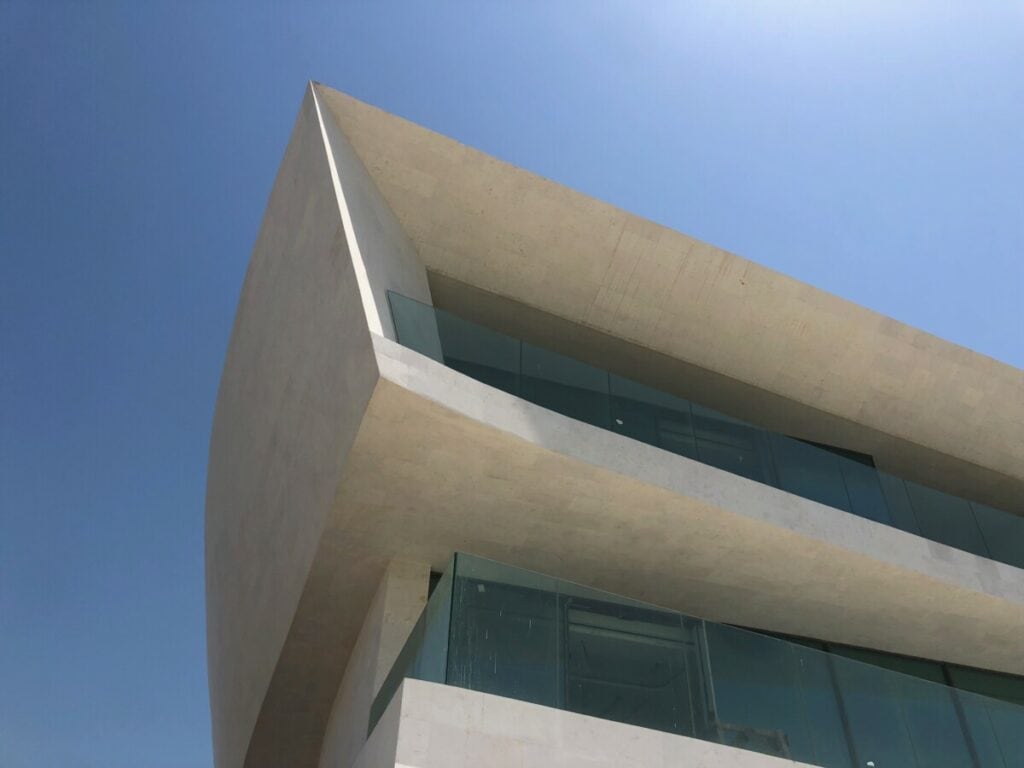 Modern architectural building with large glass windows and overhangs against a blue sky.