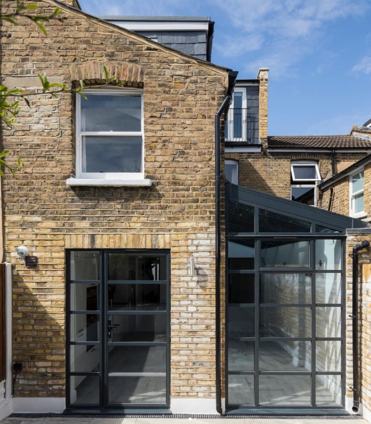 Rear view of a two-story house with traditional brickwork and modern glass elements.