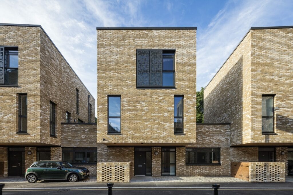 Modern residential street with minimalist townhouses, light brown bricks, and large asymmetrical windows.