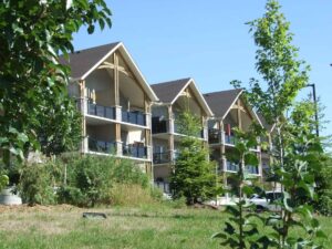 Modern apartment buildings with gable roofs, large windows, and landscaped surroundings on a sunny day.