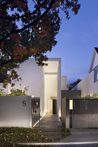 Modern minimalist house entrance with soft lighting and greenery at twilight.