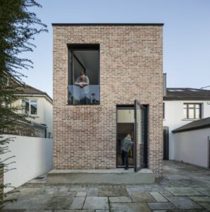 Modern, minimalist two-story brick house with large windows and black-framed glass door.