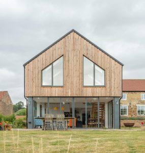Contemporary A-frame house with wooden cladding and expansive glass windows in a tranquil setting.