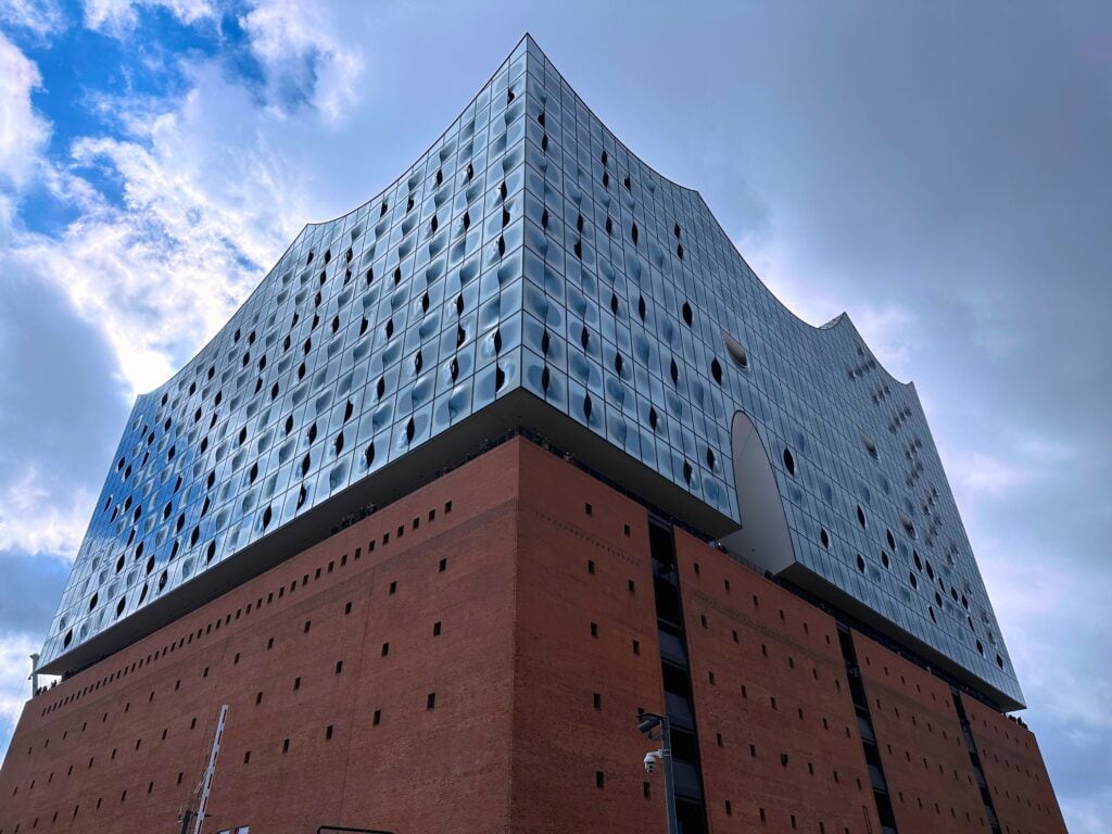 Modern building with brick base and undulating glass facade reflecting sky.