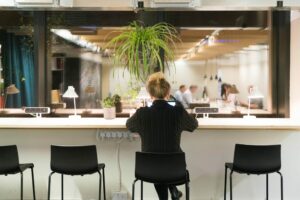 Person working alone at cafe counter, contrasting collaborative group in background. Modern, well-lit workspace.