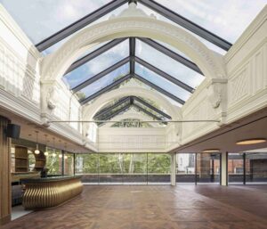 Elegant modern-classical interior by Benedetti Architects with glass ceiling, parquet floor, and gold-toned bar.