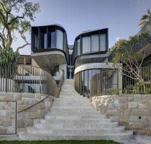 Contemporary curvilinear home blending with nature, featuring glass façades and lush landscaping.