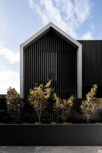 Modern black timber house with gabled roof, large windows, and tranquil landscaped surroundings.