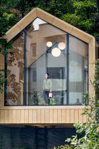 Contemporary wooden home with large windows, nestled in lush greenery, inviting nature indoors.