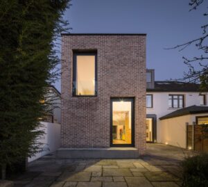 Modern brick house extension with large windows at dusk.