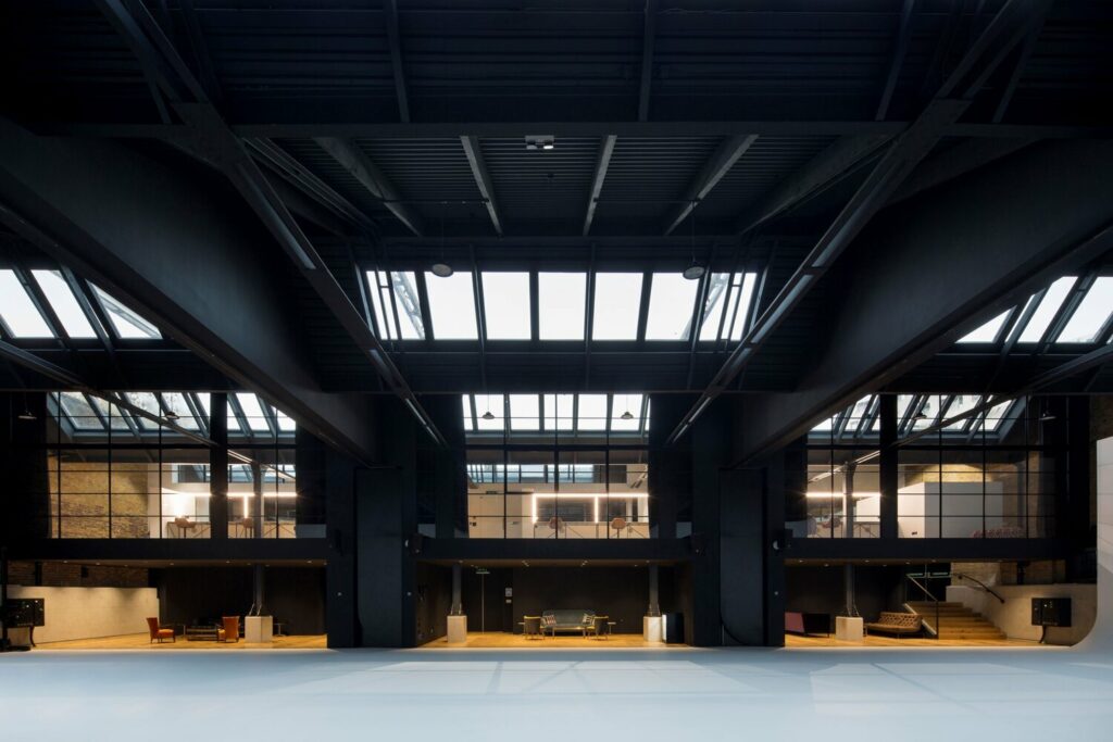 Modern industrial interior with skylights, grid-like beams, large windows, and concrete floors.