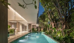 Luxurious modern pool area by contemporary house with glass windows and lush greenery.