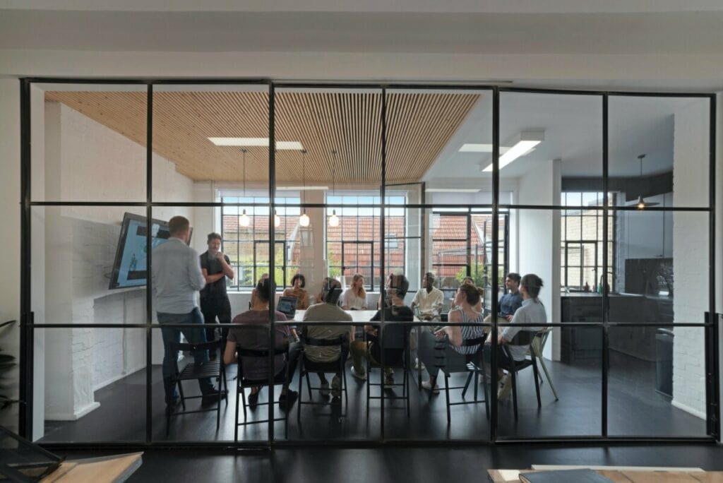 Modern meeting room with discussion, glass walls, natural light, and digital presentation screen.