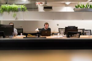 Modern industrial office with shared wooden desk, tech workstations, and green plants for a balanced workspace.