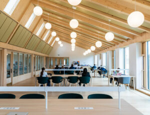 Modern study room with high ceilings, natural light, wooden beams, and collaborative workspace.