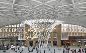 Grand train station with modern white lattice roof and classical facade bustling with activity.