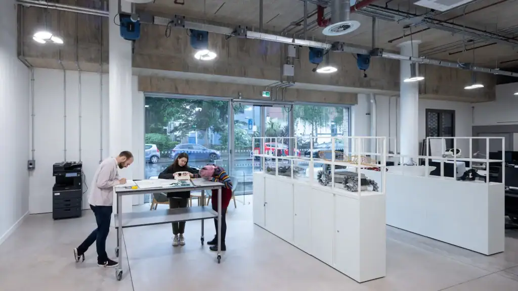 Modern, spacious workspace with natural light, high ceilings, and collaborative activities around a tall table.