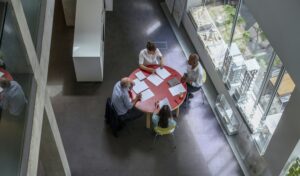 Modern office meeting around a red table with natural light and sleek design.