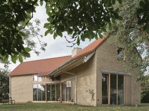 Modern brick house with terracotta roof, large glass windows, and lush lawn.