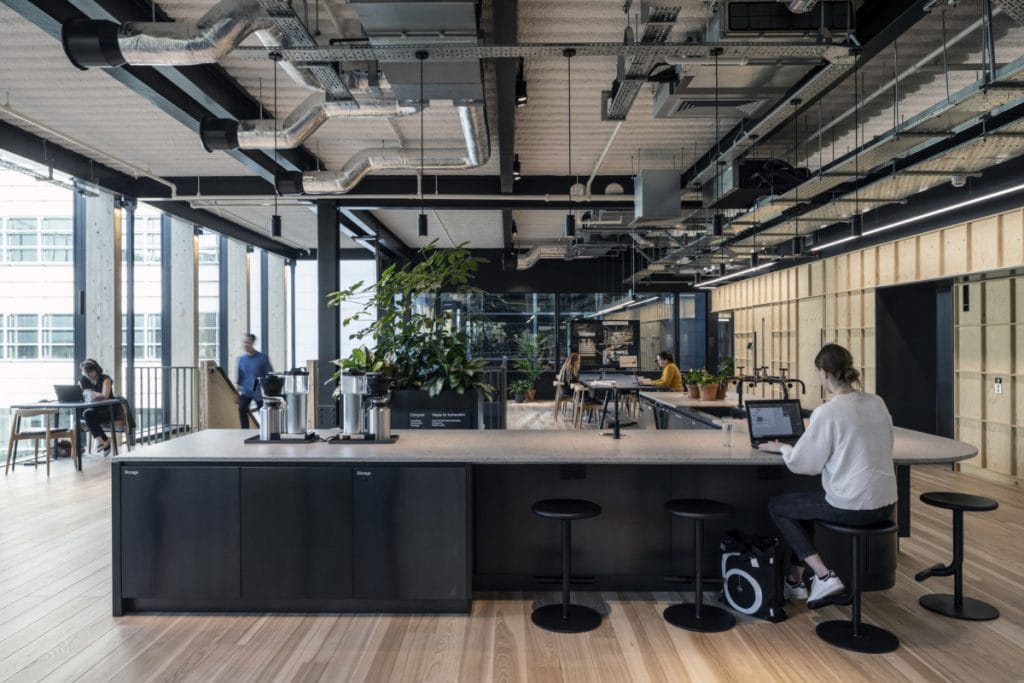 Modern open-plan office with industrial design, communal workspace, and abundant natural light.