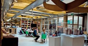 Modern industrial office space with meeting area, bookshelf, lounge, and architectural displays. Bright, airy, collaborative.