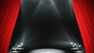 Theatre stage with red curtains and spotlights awaiting performance.