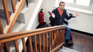 Man in wheelchair faces inaccessible stairs, looking frustrated.