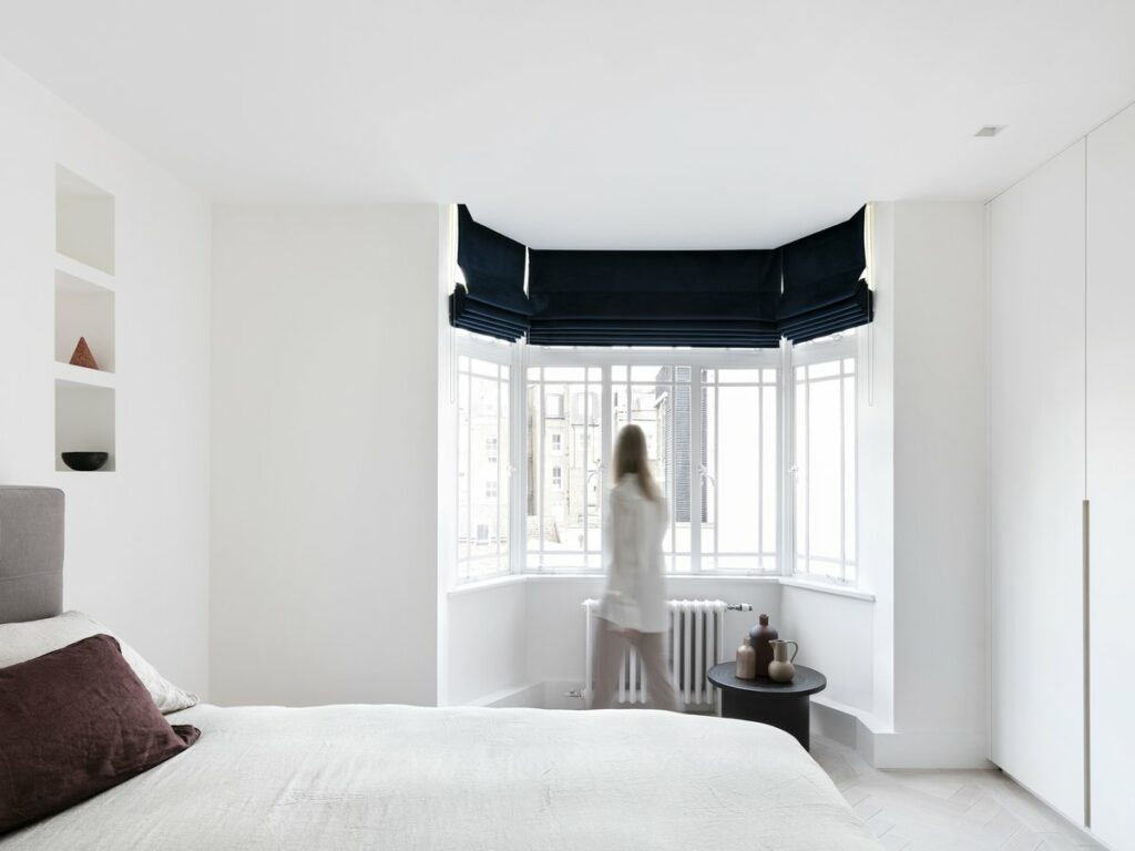 Minimalist bedroom with white walls, large bed, bay window, and built-in shelving unit.